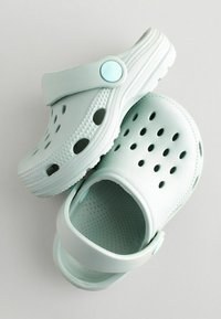 Zoccoli azzurri chiari in plastica testurizzata, con punta chiusa, fori di ventilazione e fascia posteriore per una vestibilità sicura.