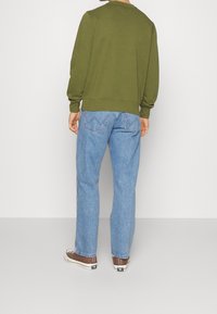 Felpa verde oliva con collo rotondo e orlo a coste, abbinata a jeans azzurri a gamba dritta e sneakers basse marroni.