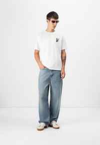 White cotton t-shirt with a small butterfly graphic on the chest, paired with light blue wide-leg denim jeans and white sneakers.