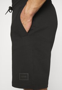 Shorts noirs en mélange de coton, dotés d'une taille élastique avec cordon de serrage, d'une poche latérale et d'un patch de marque près de l'ourlet.