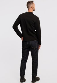 Svart långärmad skjorta med krage, matchad med mörkblå jeans. Jeansen har gul sömnad och en slim fit-design. Svarta stövlar fulländar outfiten.
