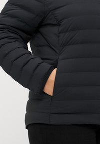 Schwarze Daunenjacke mit gestepptem Design, auffälliger Naht, seitlichen Taschen und einer glatten, matten Oberfläche.
