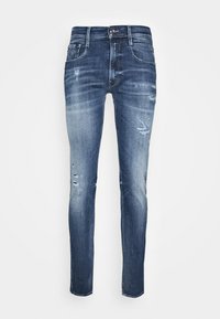 Úzké modré džíny z denimu s vybledlými oblastmi, poškozenými detaily na stehně a klasickým pětikapsovým designem se zapínáním na kovový knoflík.