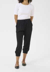 Černé, lehké teplákové kalhoty s manžetami u kotníků a elastickým pasem, doplněné těsným bílým tričkem s krátkým rukávem a černými balerínami.