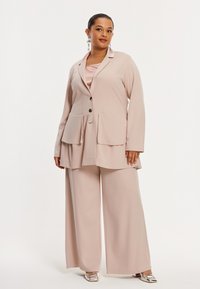 Roze getinte blush pakset met een op maat gemaakte blazer, voorzien van een gelaagd ontwerp en twee voorzakken, gecombineerd met wijde broekspijpen.