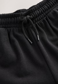 Primo piano della vita di pantaloni della tuta neri con fascia elastica e coulisse nera annodata a fiocco.