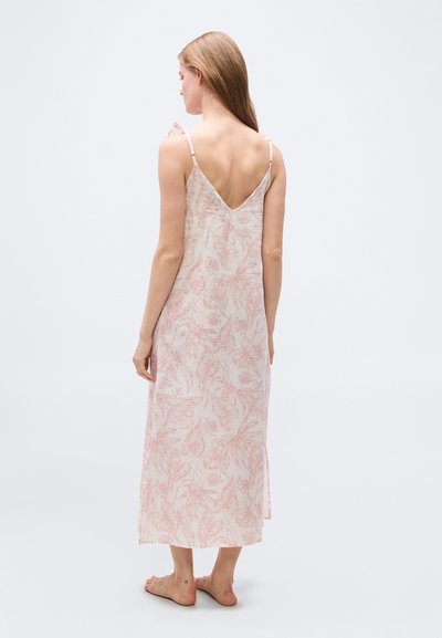 Γυναίκα με μακριά μαλλιά που φοράει αμάνικο midi φόρεμα σε ανοιχτό ροζ με floral σχέδιο και βαθύ V στην πλάτη, όρθια ξυπόλυτη σε λευκό φόντο.