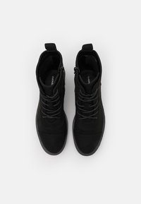 Une paire de bottines en suède noir à lacets avec des zips sur les côtés, vues de dessus sur un fond blanc.