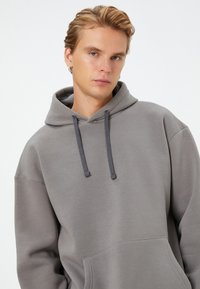 Gray hooded sweatshirt made from soft fabric, featuring a kangaroo pocket, drawstrings in a darker shade, and relaxed fit.