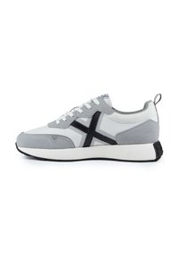 Zapatilla gris claro con detalles en blanco y negro. Material de ante y textil, puntera redondeada, suela plana y un lazo en el talón para ponérselas fácilmente.
