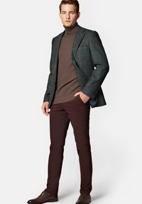 Ciemnozielony marynarka w kratę nałożona na brązowy sweter z golfem o prążkowanej fakturze, zestawiona z wąskimi bordowymi spodniami i brązowymi butami eleganckimi. Dopasowany krój, strukturalny fason.