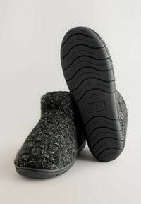 Grijze gebreide sloffen met een gestructureerde bovenkant en een zwarte rubberen zool met een golfpatroon, gemarkeerd met maat 8/42.