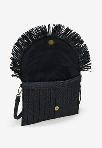 Bolso de mano tejido en negro con parte superior con flecos, cuenta con un cierre de botón y una correa desmontable. El interior está forrado con tela negra.