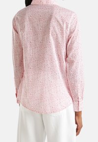 Dlouhý rukáv košile z světle růžové tkaniny s květinovým vzorem. Obsahuje klasický límec a manžety na knoflíky, s zakřiveným lemem.