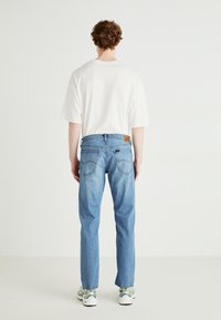 Ljusblå jeans med bakfickor, rak bendesign och en ljusbrun läderlogga. Bärs med en lös passande vit t-shirt.