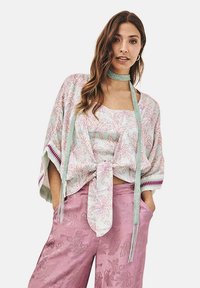 Kimono ligero en menta con patrones de hojas rosas, atado a la cintura, combinado con pantalones sueltos rosas que presentan una sutil textura floral.