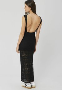 Robe maxi en dentelle noire avec un dos décolleté et une coupe sans manches, présentant une silhouette ajustée et un détail en dentelle texturée.