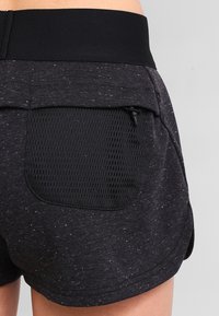 Mustat shortsit, joissa on teksturoitu kuviointi, leveä vyötärönauha ja verkkovuorinen takatasku. Kankaassa on vaaleampia pilkkuja.