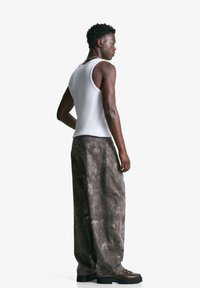Hvid tanktop og stenvaskede brune bukser med brede ben lavet af denim, med synlige sømme, tekstureret overflade og støvler med sort sål.