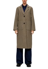Lange jas met houndstooth-patroon in bruin en beige, voorzien van een notch lapel, twee voorzakken en zwarte knopen. Gecombineerd met donkerblauwe broek.