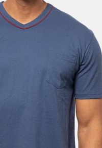 Blå T-shirt med V-hals, rød accentkant og en brystlomme til venstre. Stoffet er blødt med en glat tekstur og korte ærmer.