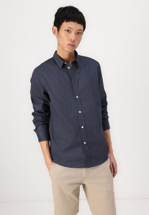 Dunkelblaues Hemd mit Knöpfen aus leichtem Stoff, mit klassischem Kragen, langen Ärmeln und taillierter Silhouette. Kombiniert mit beigen Shorts.