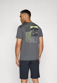 Grå kortermet t-skjorte med et kart-inspirert grafisk design i grønt, svart og hvitt på baksiden. Kombinert med mørke shorts som gir en avslappet passform.