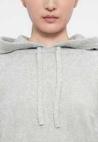 Hellgrauer Hoodie mit geripptem Kragen, Kordeln und strukturiertem Stoff. Das Design bietet eine klassische Passform und eine weiche Textur.