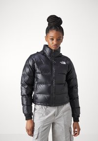 Črna napihnjena jakna z visokim ovratnikom, zadrgo in prešito zasnovo. Ima logotip na levi prsni strani in rebraste manšete.