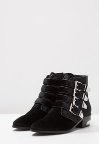 Stivali neri alla caviglia in camoscio testurizzato, caratterizzati da quattro cinturini metallici con fibbia, punta appuntita e tacco basso a blocco.