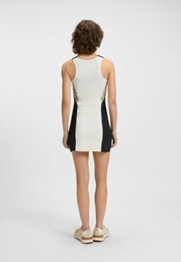 Ärmelloses Kleid in Creme, Schwarz und beige mit Farbblockdesign. Hat eine figurbetonte Silhouette und einen weichen, glatten Stoff. Wird mit hellen Schuhen getragen.