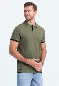 Olivově zelené polo tričko s klasickým límečkem, černými akcenty na rukávech a třemi knoflíky. Měkká textura a decentní logo značky na lemu.