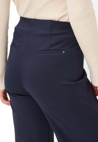 Navy blue trousers with a smooth texture, featuring a back pocket and a small metallic accent. The waistband is tailored and fitted.