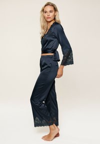 Marine satijnen pyjama set met kanten accenten; bevat een langwerpig shirt en bijpassende broek met kanten zoom. Zachte, gladde textuur.
