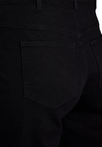 Vaqueros de denim negro con una silueta ajustada, que cuentan con un único bolsillo trasero y detalles de costura sutiles. Tejido texturizado con un acabado mate.