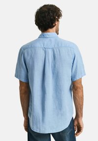 Camisa de lino ligera de manga corta en color azul claro, con un detalle de ventilación en la parte posterior y un cuello con botones. Textura suave, ajuste relajado.