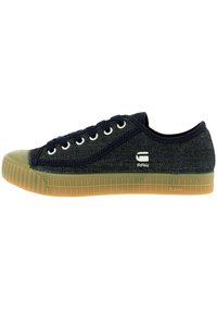 Dark blue canvas sneaker with round toe, rubber sole, white eyelets, and side logo detail. Features textured fabric and contrasting green accents.
