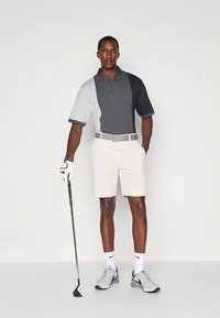 Golfpolo i grå og svarte fargeblokker, kombinert med lyse beige shorts. Tilbehør inkluderer golfhanske og kølle, med sportssko.