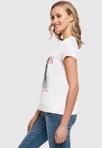 Hvid bomulds t-shirt med korte ærmer, rund halsudskæring og et grafisk print med rød tekst og designdetaljer på forsiden.