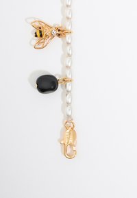 Bracciale di perle con un charm a forma di ape in oro con strass, una pietra nera e una chiusura in oro con testo inciso.