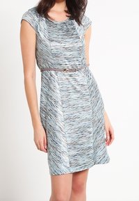 Une robe ajustée à manches courtes en tissu texturé avec un motif ondulé bleu. Fini avec une ceinture marron à la taille pour plus de détails.