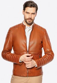 Braune Lederjacke mit hohem Kragen, Reißverschluss, gerippten ÄrmelDetails und Seitentaschen. Glatte Textur und taillierte Passform.