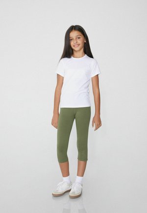 T-shirt bianco a maniche corte abbinato a legging verdi, calzini bianchi e sneakers chiare. Design semplice con una palette di colori neutri.