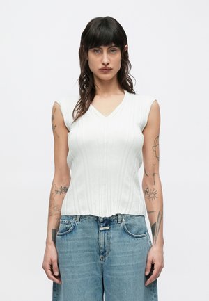 Haut blanc côtelé avec un col en V et des manches courtes, doté d'une coupe ajustée et d'une texture subtile. Associé à un jean en denim bleu clair.