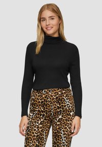 Zwarte coltrui met lange mouwen, gecombineerd met broek met een bruin en zwart luipaardpatroon, voorzien van een gladde textuur en voorzakken.