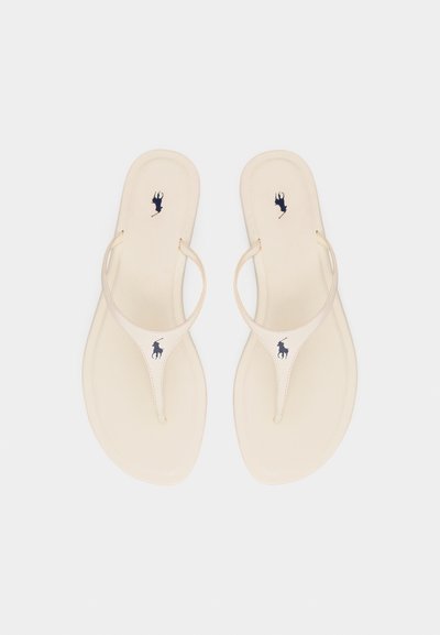 Μπεζ σανδάλια τύπου thong με λεπτές λουρίδες και σκούρο λογότυπο παίκτη πόλο στο πέλμα και στο λουρί, εμφανιζόμενα από πάνω σε λευκό φόντο.