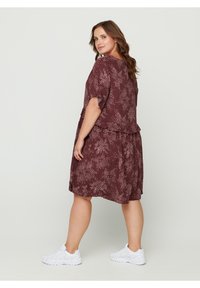 Robe florale bordeaux à manches courtes et design superposé. Fabriquée en tissu léger, elle présente une coupe décontractée et une longueur au genou. Portée avec des baskets blanches.