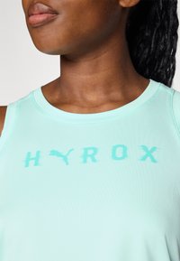 Lyse mintgrønn trenings tanktop med rund hals, prydet med ordet "HYROX" og en katte-logo i en litt mørkere nyanse. Glatt tekstur.