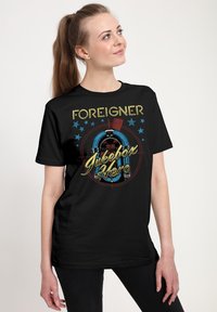 Czarna koszulka z grafiką retro jukeboxa oraz napisem "FOREIGNER Jukebox Hero" w żółtym i niebieskim kolorze, z akcentami w postaci niebieskich gwiazdek.