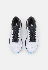Zapatillas de correr blancas con cordones negros y un collar negro texturizado. Presentan acentos en azul y plata, además de una parte superior perforada para la transpirabilidad.